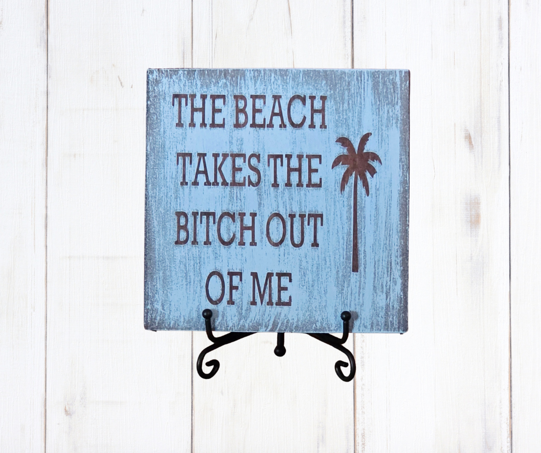 The Beach Takes The Bitch Out Of Me sign on blue teal wood