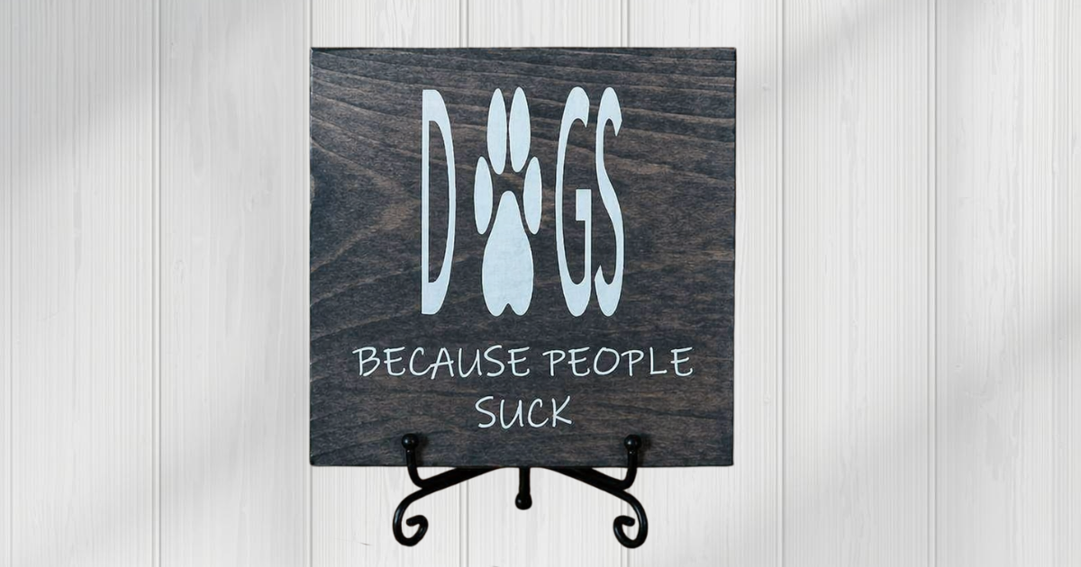 Dogs Because People Suck sign on dark charcoal pine